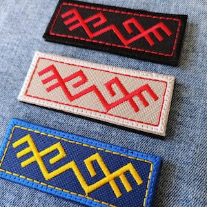 May include: Three rectangular embroidered patches featuring a geometric zigzag pattern. The top patch is black with red stitching, the middle is beige with red stitching, and the bottom is blue with yellow stitching, all with matching borders.