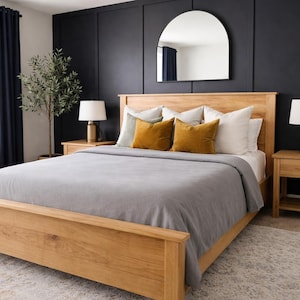 May include: A light wood bed frame with a gray comforter and mustard-colored pillows. The bedroom features a dark blue accent wall, a large arched mirror, and matching wooden nightstands with lamps.