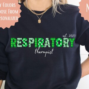May include: Navy blue sweatshirt with the words "RESPIRATORY therapist" in green, with white accents and the text "est. 2023". The sweatshirt also has the text "MANY COLORS TO CHOOSE FROM & PERSONALIZED" and "LISTING FOR SHIRT ONLY".