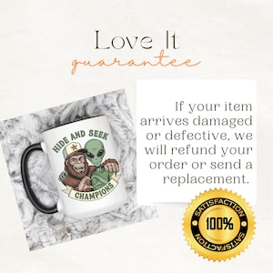 May include: A white ceramic mug with a black handle featuring a graphic of a brown Bigfoot and a green alien wearing a baseball cap with the text Hide and Seek Champions. The image includes text about a refund policy and a 100% satisfaction seal.
