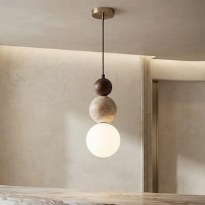 May include: A pendant light fixture suspended from a brass ceiling canopy by a thin rod. The fixture features a vertical stack of three spheres: a dark brown wooden sphere, a textured beige stone sphere, and a smooth white frosted glass globe.