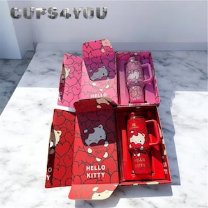 May include: Two Hello Kitty themed Stanley tumblers in their original boxes. One is red with a white Hello Kitty design, and the other is pink with a Hello Kitty design. The boxes are pink and red with Hello Kitty and heart designs.