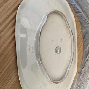 May include: An off-white, oval serving platter with a scalloped edge. The underside is visible, showing a stamp that reads "H. BEQUET, Quaregnon, Belgium" and the number "537". The platter is resting on a wooden surface.