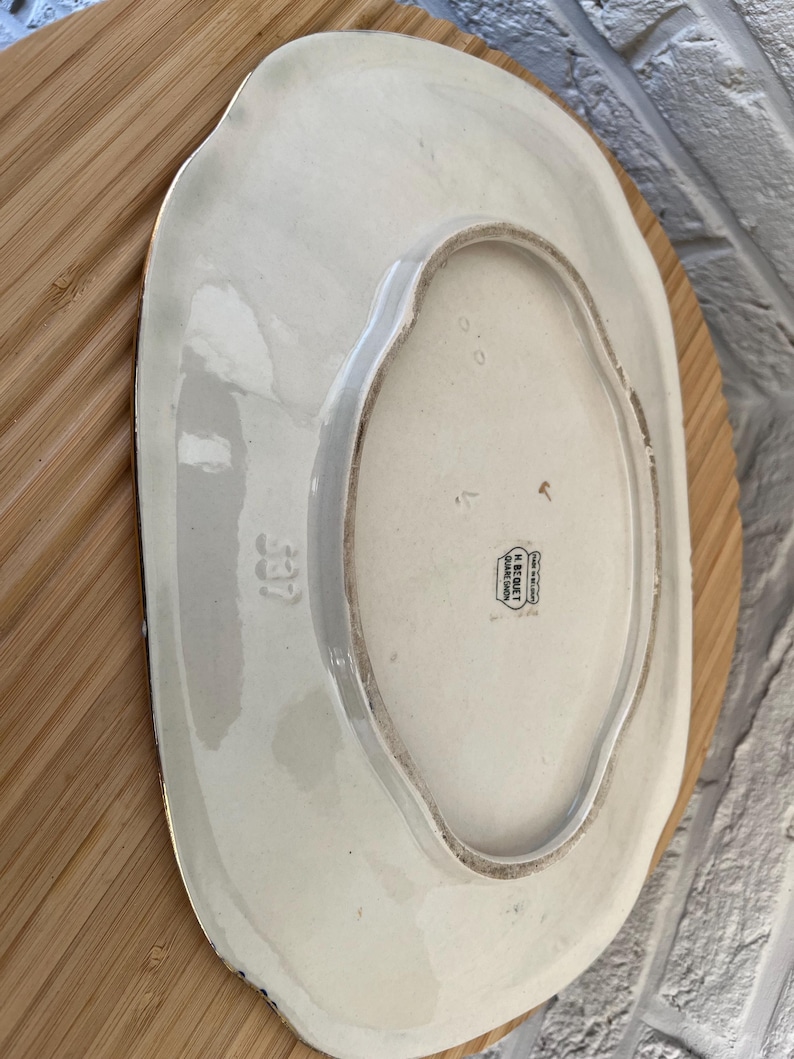 May include: An off-white, oval serving platter with a scalloped edge. The underside is visible, showing a stamp that reads "H. BEQUET, Quaregnon, Belgium" and the number "537". The platter is resting on a wooden surface.