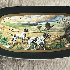 Puede incluir: Bandeja rectangular con borde verde oscuro y borde interior dorado. La bandeja presenta una pintura detallada de perros de caza y faisanes en un campo con un fondo de cielo nublado.