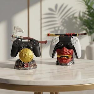 May include: Two game controller stands. One black controller has a silver axe on top and a gold disc below. The other white controller has a red and gold mask below and a sword on top. Both are on a white table.