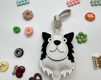 May include: A white and black leather dog-shaped keychain with a cream-colored strap. The keychain is surrounded by colorful decorative food-shaped embellishments, including donuts, flowers, and pretzels.