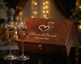Op de afbeelding: Twee champagneglazen en een houten kist. De glazen zijn gegraveerd met de namen "David" en "Olivia", samen met de datum "28 juni 2026" en hartontwerpen. De houten kist is ook gegraveerd met de namen en datum.