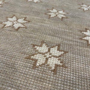 May include: Close-up of a beige rug with a repeating pattern of star-shaped designs in off-white and brown. The rug has a textured surface, and the stars are evenly spaced across the fabric.