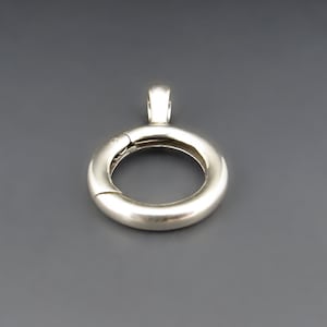 May include: Silver-toned pendant with a circular design. The pendant has a hinged opening and a loop at the top for attaching to a chain.