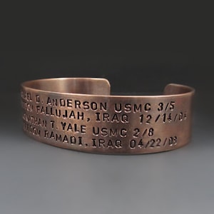 May include: A copper bracelet engraved with the names "Chel D. Anderson USMC 3/5" and "Nathan T. Yale USMC 2/8" along with their deployment dates and locations: "Fallujah, Iraq 12/14/04" and "Ramadi, Iraq 04/22/03".