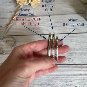 May include: Three silver-colored metal cuffs of varying thicknesses are displayed. Text labels identify them as a Heavy 4 Gauge Cuff, an Original 6 Gauge Cuff, and a Skinny 8 Gauge Cuff. The Heavy 4 Gauge Cuff is highlighted as the item in this listing.