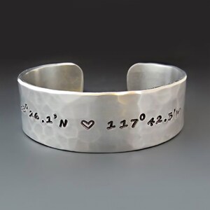 May include: A silver hammered cuff bracelet with the coordinates "26.1° N ♥ 117° 42.5'" engraved on it.
