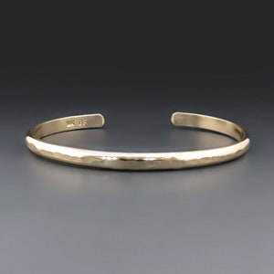May include: A gold hammered cuff bracelet. The bracelet is simple and elegant, with a smooth, polished finish. The bracelet is marked "14K GF" on the inside.
