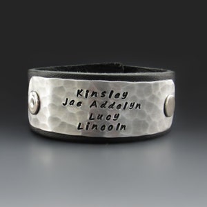 May include: Black leather bracelet with a silver hammered metal plate engraved with the names Kinsley, Jae, Addelyn, Lucy, and Lincoln.