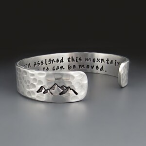 May include: Silver bracelet with a hammered finish and the inscription "If you can assigned this mountain it can be moved."  The bracelet features a small mountain silhouette.