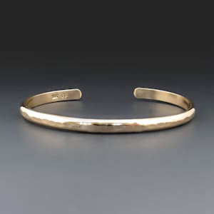 May include: A gold hammered bangle bracelet. The bracelet is simple and elegant, with a smooth, polished finish.