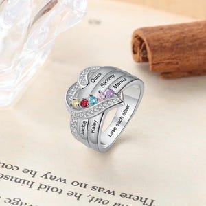 May include: A silver heart-shaped ring with colourful gemstones and the names "Quick", "Sammy", "Mamie", "Jackie", and "Kaley" engraved on it. The ring also has the inscription "Love each other".