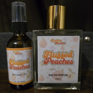 May include: A 60 ml amber glass bottle of dry body oil with a black spray pump and a 100 ml clear glass bottle of eau de parfum with a gold cap. Both bottles feature white labels with peach illustrations and the text Fluffed Peaches.