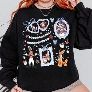 Puede incluir: Sudadera negra con personajes de Disney enmarcados. Mickey y Minnie Mouse, el Pato Donald, Goofy y Pluto se representan con elementos náuticos. También está presente el texto "Disney Cruise Line".
