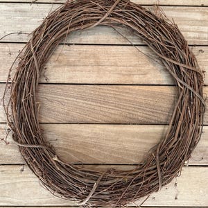 Könnte beinhalten: Ein kreisförmiger Kranz aus braunen Weinreben, mit einem natürlichen, rustikalen Aussehen. Der Kranz besteht aus ineinander verschlungenen Ranken, die eine volle, strukturierte Erscheinung erzeugen. Ideal für saisonale Dekorationen oder Bastelprojekte.