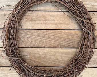 May include: A circular grapevine wreath, showcasing a natural, rustic aesthetic. The wreath is composed of intertwined brown vines, creating a full, textured appearance. Ideal for seasonal decor or crafting projects.