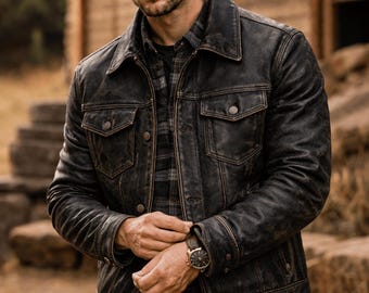Può includere: Giacca in pelle nera invecchiata con due tasche sul petto e chiusure con bottoni. La giacca è indossata sopra una camicia a quadri e jeans scuri. Un orologio dorato con quadrante nero è visibile al polso.