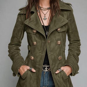Könnte beinhalten: Eine olivgrüne zweireihige Jacke mit breitem Reverskragen, Schulterklappen und metallisch goldfarbenen Knöpfen. Die Jacke hat lange Ärmel mit gerippten Bündchen und wird über einem schwarzen Oberteil und einer blauen Jeans getragen.