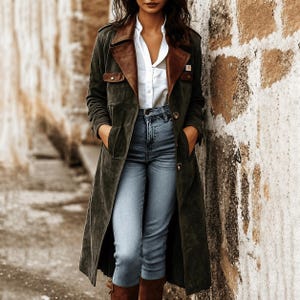 May include: A long olive green suede trench coat with brown leather lapels and buttoned chest pockets, worn over a crisp white button-down shirt and light blue denim jeans. The coat features a structured collar and visible buttons down the front.