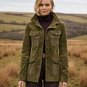May include: An olive green suede jacket featuring a structured collar, a button-front closure, and four front pockets. The upper and lower pockets are accented with a brown and green plaid fabric pattern. The jacket is worn over a dark purple turtleneck.