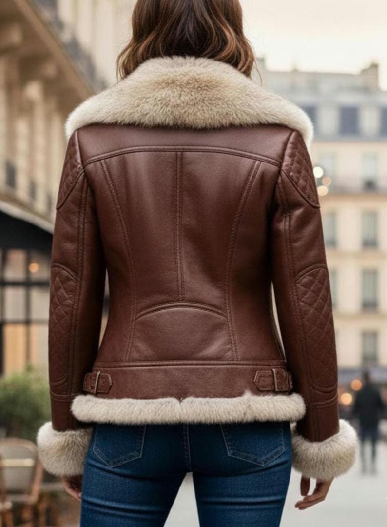 Puede incluir: Chaqueta de cuero marr&oacute;n con cuello, pu&ntilde;os y dobladillo de piel color crema. La chaqueta presenta detalles acolchados en los hombros y los brazos, y un cintur&oacute;n con hebilla en la cintura. El modelo lleva vaqueros azules.