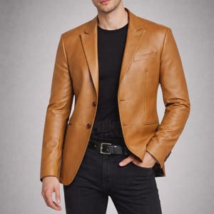 May include: A tan leather blazer with a two-button closure, a notched lapel, and a chest pocket. The blazer is worn over a black t-shirt and paired with black pants and a black belt.