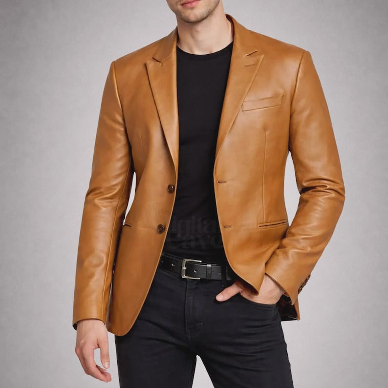 May include: A tan leather blazer with a two-button closure, a notched lapel, and a chest pocket. The blazer is worn over a black t-shirt and paired with black pants and a black belt.