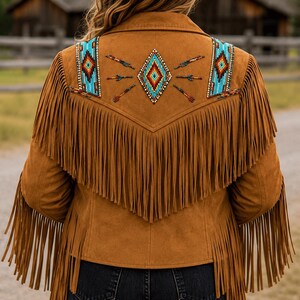 May include: A tan suede jacket featuring long fringe detailing across the back and sleeves. The upper back panel is decorated with intricate beadwork in geometric diamond and arrow patterns using vibrant blue, red, orange, and white glass beads.