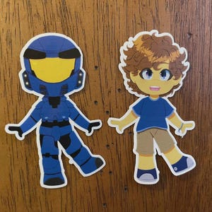 May include: Two cartoon stickers on a wooden surface. One is a blue armored figure with a yellow visor. The other is a cartoon boy with brown curly hair, a blue shirt, and khaki shorts. Both have white outlines.