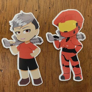 May include: Two cartoon stickers. One features a character with gray hair, a red shirt, black shorts, and a weapon. The other is a red armored figure with a yellow visor, also holding a weapon.