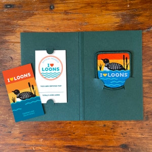 May include: A green card holder with a white card inside that says "Official Member I ♥ Loons This card certifies that totally loves loons" and a green patch with a loon on it that says "I ♥ Loons".