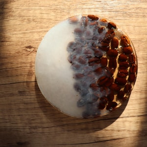 Może przedstawiać: Okrągły podkładka z podzielonym wzorem. Jedna połowa jest biała, druga wypełniona brązowymi ziarnami kawy. Podkładka leży na drewnianej powierzchni, a światło tworzy cienie.