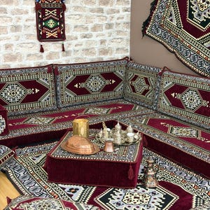 Peut inclure: Un ensemble de salon de sol bordeaux et crème avec des coussins assortis et une table basse. La table contient un plateau avec de petites tasses à thé argentées et un plat de service en cuivre. Un sac décoratif suspendu est visible.