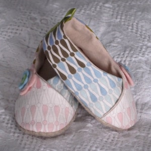 K&ouml;nnte beinhalten: Ein Paar Babyschuhe mit einem rosa-wei&szlig;en gemusterten Stoff auf dem einen Schuh und einem blau-wei&szlig;en gemusterten Stoff auf dem anderen Schuh. Die Schuhe haben ein hellbraunes Stofffutter und eine gr&uuml;ne Stoffschlaufe oben.