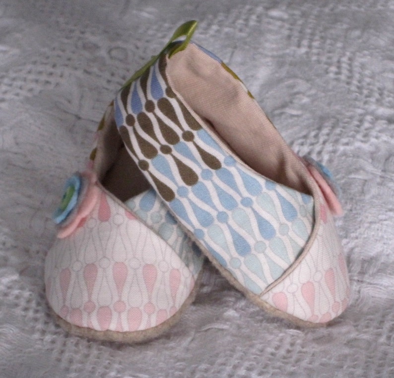 K&ouml;nnte beinhalten: Ein Paar Babyschuhe mit einem rosa-wei&szlig;en gemusterten Stoff auf dem einen Schuh und einem blau-wei&szlig;en gemusterten Stoff auf dem anderen Schuh. Die Schuhe haben ein hellbraunes Stofffutter und eine gr&uuml;ne Stoffschlaufe oben.