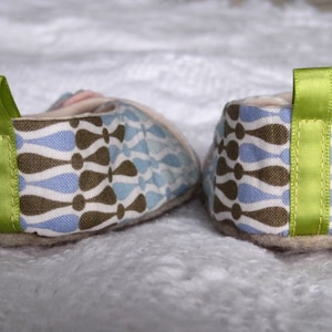 K&ouml;nnte beinhalten: Ein Paar blaue, braune und wei&szlig;e gemusterte Stoff-Babyschuhe mit gr&uuml;nem Bandbesatz.