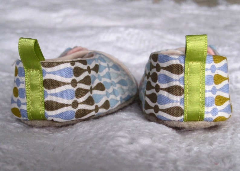 K&ouml;nnte beinhalten: Ein Paar blaue, braune und wei&szlig;e gemusterte Stoff-Babyschuhe mit gr&uuml;nem Bandbesatz.