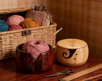 Peut inclure: Un bol à laine en bois foncé contenant une pelote rose avec un crochet, à côté d'un bol en bois clair gravé de fleurs, un panier en osier rempli de laine, une paire de ciseaux en métal et une règle en bois graduée en centimètres.