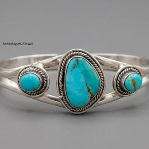 May include: Silver cuff bracelet with three turquoise stones. The central stone is an irregular oval, flanked by two round stones. The turquoise is a bright blue-green, set in a detailed silver setting. The bracelet is a piece of jewellery.