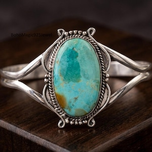 May include: A silver cuff bracelet featuring a large, oval-shaped turquoise stone with brown matrix inclusions. The stone is set in a twisted rope border with decorative silver bead accents. The band splits into two smooth, polished silver arms.