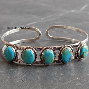 May include: A silver cuff bracelet featuring five oval turquoise stones set in twisted rope bezels. The band has a textured, etched pattern along the metal surface. The text BohoMagic925Jewel is visible in the upper left corner of the image.