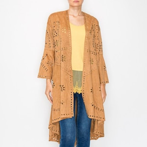 May include: A woman wearing a long, open-front, tan suede jacket with floral cutouts and bell sleeves. She is wearing a yellow top, blue jeans, and tan sandals. The jacket has a tiered design.