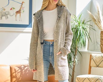 May include: A long, hooded cardigan in a neutral speckled knit with a contrasting black and white patterned hood lining. The cardigan has pockets and is worn with a white top and blue jeans. The model is wearing knee-high tan boots.