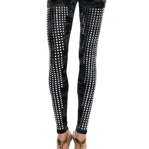 May include: Black leggings with a textured, mottled pattern and a grid-like design of silver squares down the legs. The leggings are paired with gold strappy sandals. The website address VOCALAPPAREL.COM is visible at the bottom.